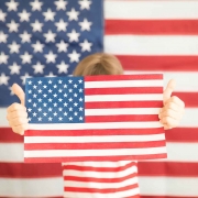 Young girl holding an American flag in front of an American flag backdrop.