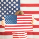Young girl holding an American flag in front of an American flag backdrop.