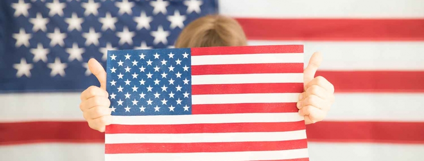 Young girl holding an American flag in front of an American flag backdrop.
