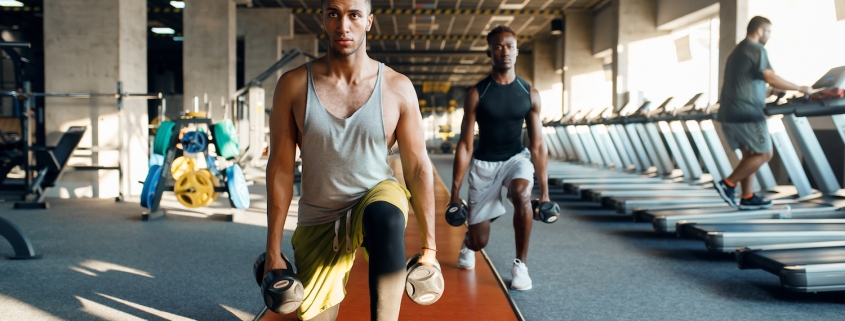 Two male persons doing exercise with dumbbells, training in gym. Fit workout in sport club, healthy lifestyle, fitness