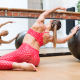 Young woman doing side stretch pilates mermaid exercises with a gym ball working out in front of a mirror in a gym