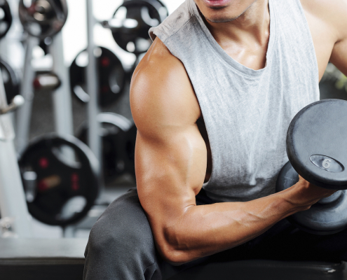 Fit strong man doing biceps curl in gym