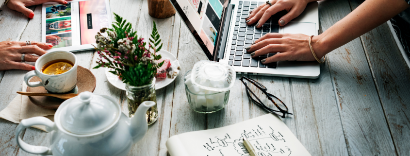 women at large table with computers, tea pot, journals