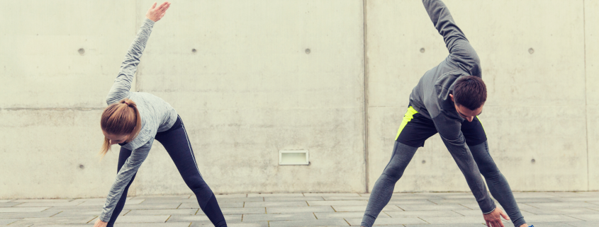 Man and woman outside in running gear stretching