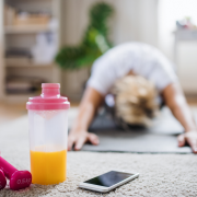 Woman stretching on the floor of her living room with weights and phone nearby.