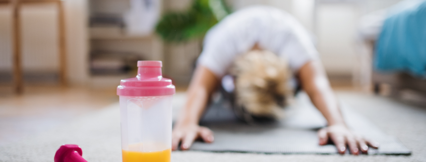 Woman stretching on the floor of her living room with weights and phone nearby.