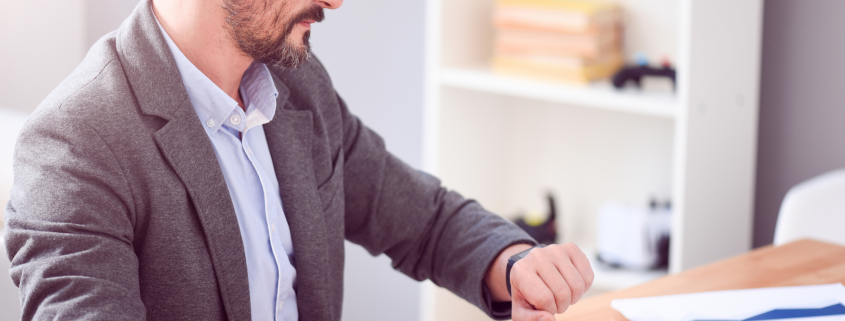 Man sitting at work desk looking at his watch.