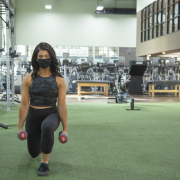 Woman holding dumbbells and performing a lunge at the gym.