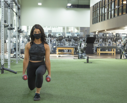 Woman holding dumbbells and performing a lunge at the gym.