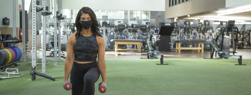Woman holding dumbbells and performing a lunge at the gym.