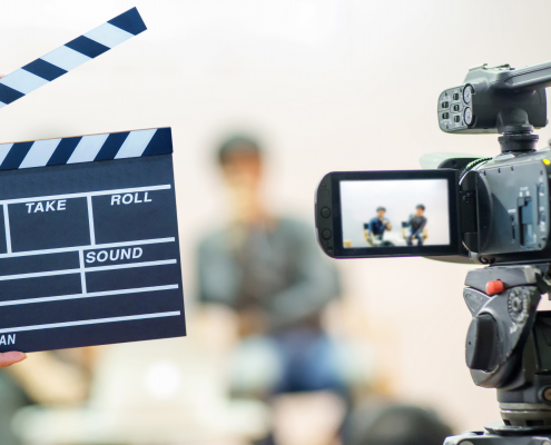 Photo of clapboard and digital camera in front of two people sitting