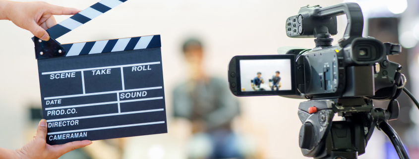 Photo of clapboard and digital camera in front of two people sitting