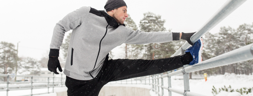 Man in his 30s stretching outside in the snow after a run