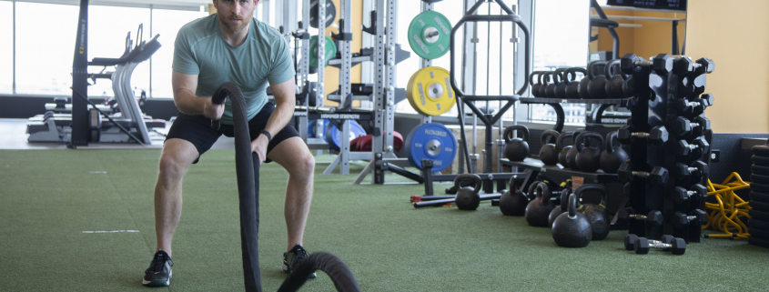 Man using battle ropes on turf inside a gym