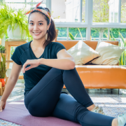 Girl stretching on a yoga mat in front of a couch and potted plants.