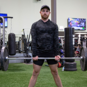 Man in gym holding barbell with weights on it.