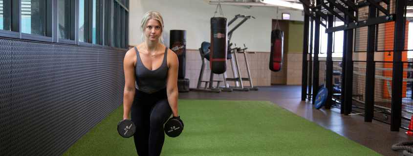 photo of woman on indoor turf in a lunging position with dumbbels