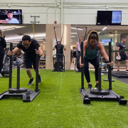 Two people on a turf pushing weighted sleds during a Faction workout class.