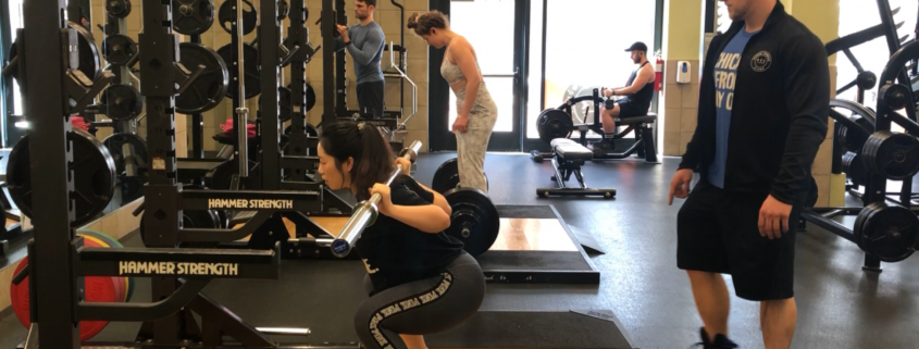 A woman at a squat rack with her trainer