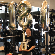 Emily With Balloons and A Trophy standing in front of a squat rack