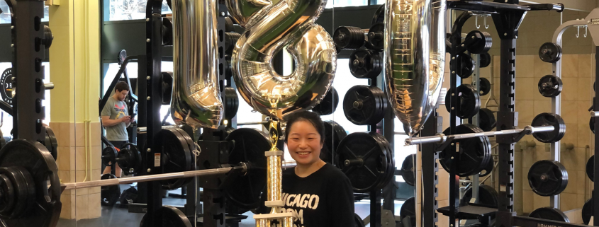 Emily With Balloons and A Trophy standing in front of a squat rack