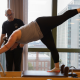 Woman stretching on a Pilates reformer machine with her Pilates trainer.