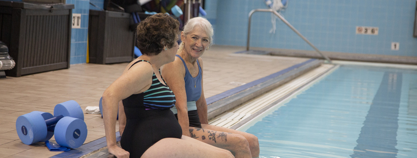 Two older women sitting on the edge of a pool