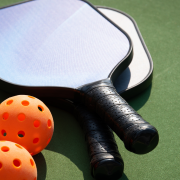 Three orange pickleballs and two paddles set on a court