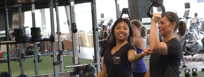 2 women working out on a turfed fitness area with kettlebells