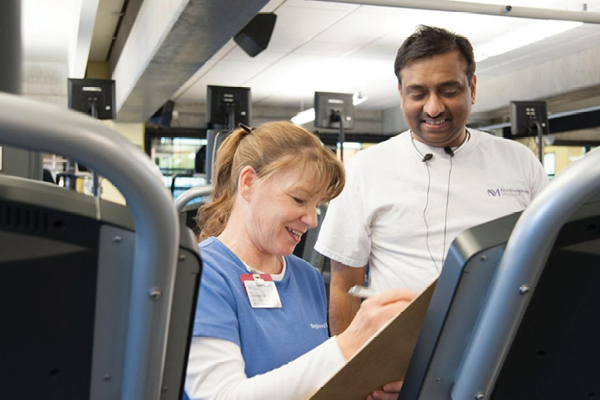 Rush employee assisting a FFC Gold Coast member on the treadmill while she takes notes on her notepad.